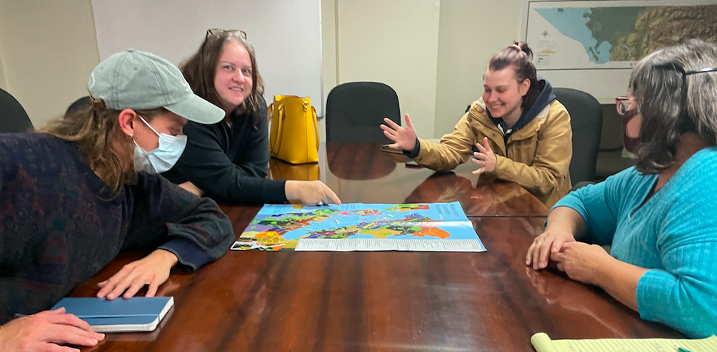 Four smiling coop members around a conference table discussing a large colorful map.